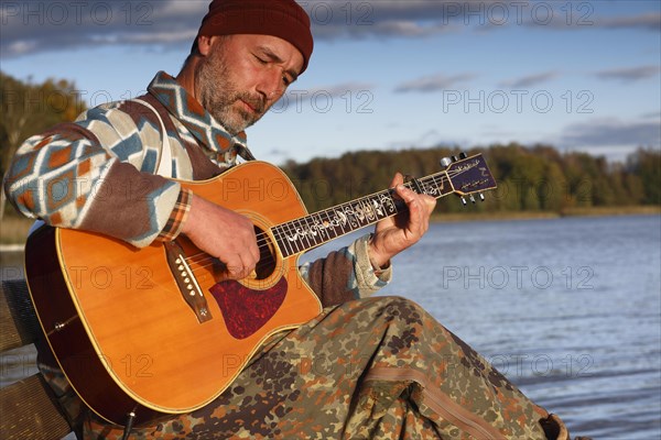 Man playing guitar on a jetty by the lake