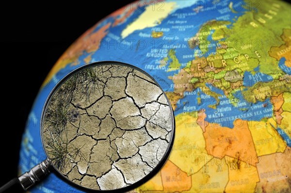 Cracked earth by drought seen through magnifying glass held against illuminated terrestrial globe