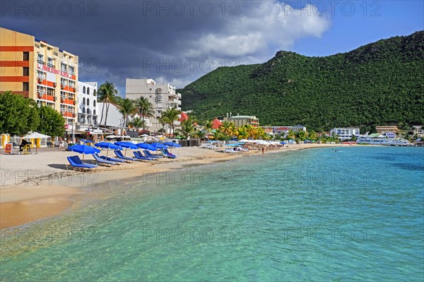 Tourists sunning on sandy beach with palm trees at Great Bay in capital city Philipsburg of the Dutch island part of Sint Maarten in the Caribbean Sea