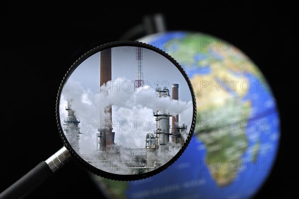 Chimneys covered in smoke seen through magnifying glass held against illuminated terrestrial globe