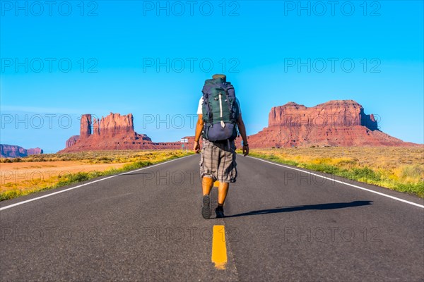 A young man walking along the road with his yellow lines of Monument Valley