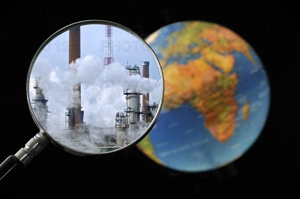 Chimneys covered in smoke seen through magnifying glass held against illuminated terrestrial globe