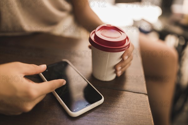 Close up girl browsing smart phone holding disposable cup