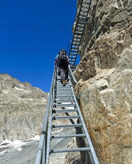 Hikers climb metal stairs up a rock face to the Konkordiahuette mountain hut