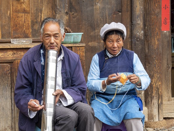 Old Chinese couple sitting in front of wooden house