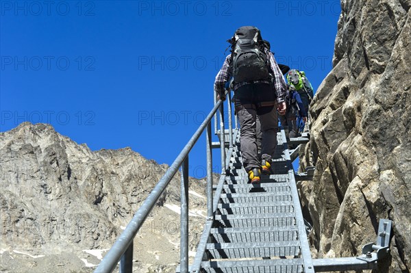 Hikers climb metal stairs up a rock face to the Konkordiahuette mountain hut