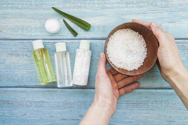 Close up hand holding bowl rock salts with aloevera spray bottles cream