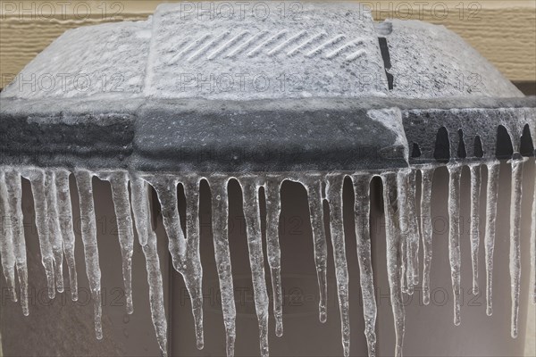 Brown and black plastic trash can covered with ice and icicles