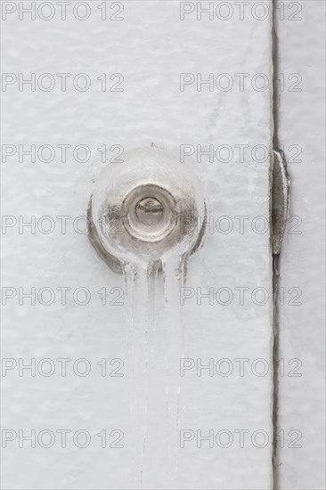 Close-up of ice covered doorknob with keyhole and strike plate on white door