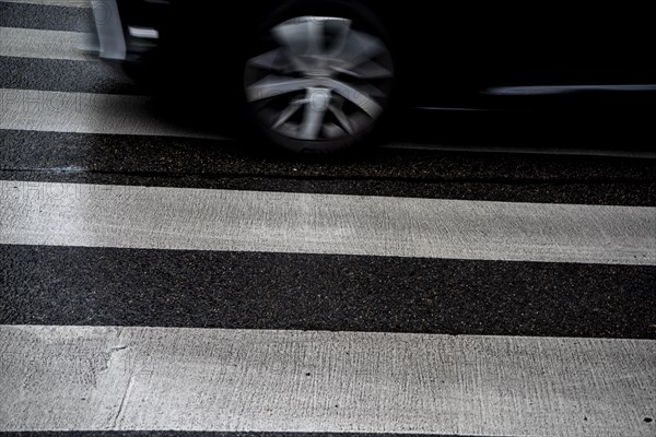 Wet zebra crossing with black fast-moving car in the background