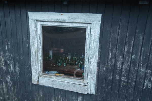 Beer bottles and cigarette packets behind the window of an old fishing hut