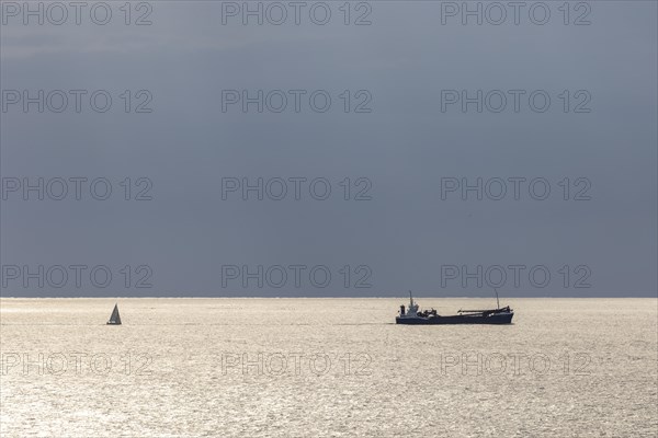 Dark clouds and sunlight and a sailboat and freighter over the North Sea