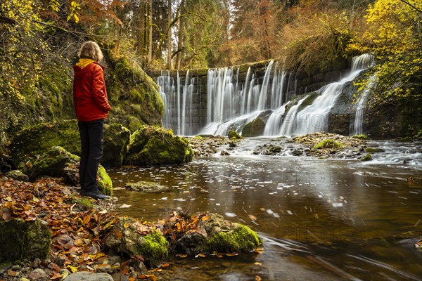 The Geratser waterfall in autumn. A hiker stands on the bank. Moss-covered rocks on the sides