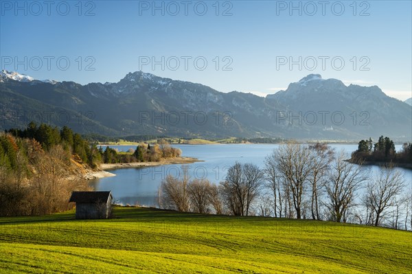 The Illasbergsee in the Allgäu in autumn in the late afternoon in good weather with a blue sky. A small hut in the foreground