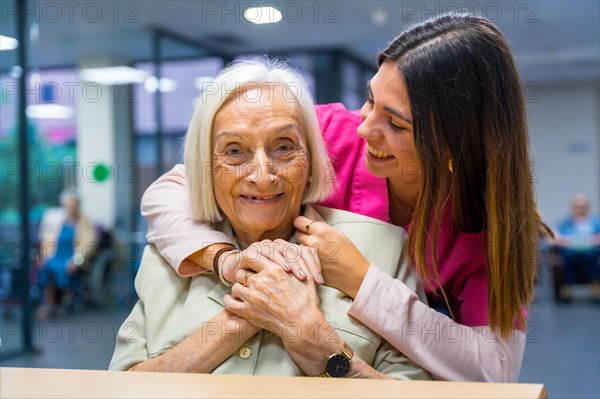 Nurse embracing from the back a cute elder woman in a geriatric