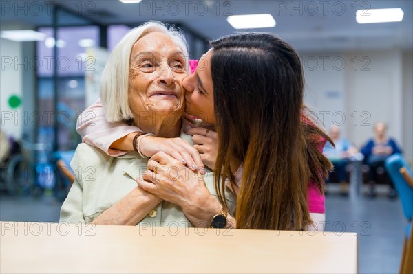 Nurse kissing and embracing from the back a cute elder woman in a geriatric
