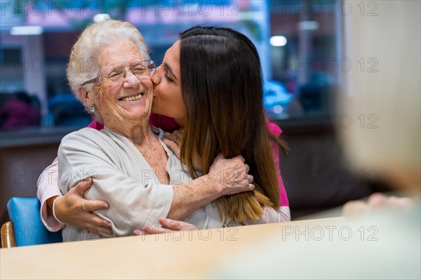 Happy moment of an elder woman and nurse embracing and kissing in a geriatric