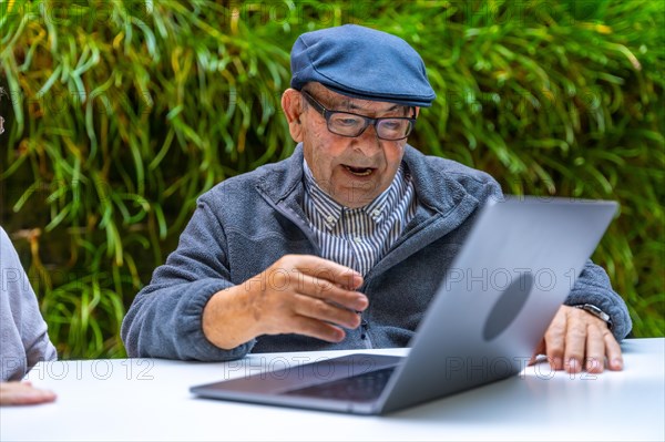 Retired old man using laptop in a garden of a nursing home
