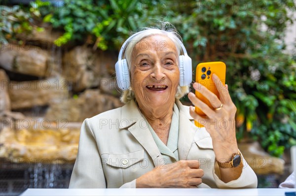 Happy elder woman using headphones and mobile to listening to music in a geriatric