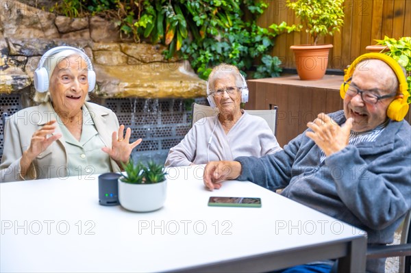 Three happy and cute seniors enjoying listening to music with headphones in a geriatric