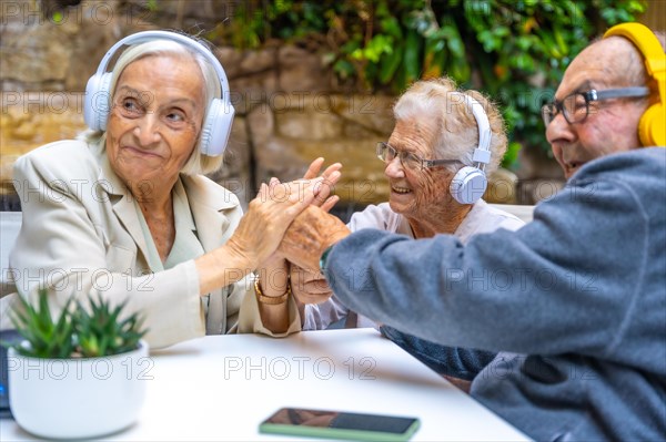 Seniors enjoying music using headphones sitting on a garden in a nursing home