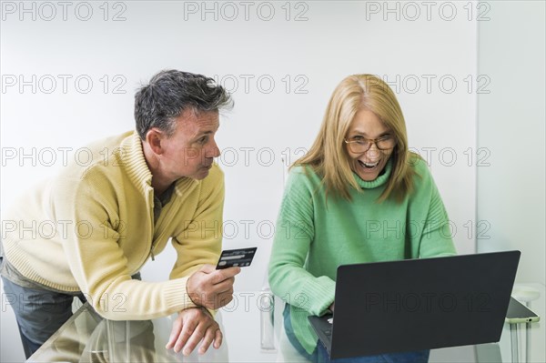 Husband and wife shopping from home using notebook and credit card