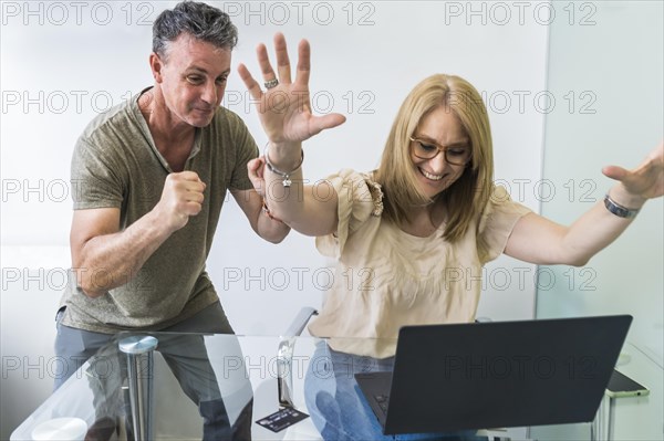 Cheerful husband and wife shopped from home using notebook and credit card while raising arms up