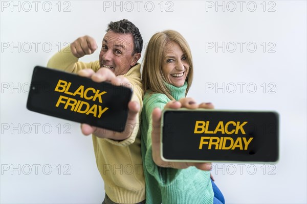 Happy couple holding smart phones with Black Friday advertisement on the screens