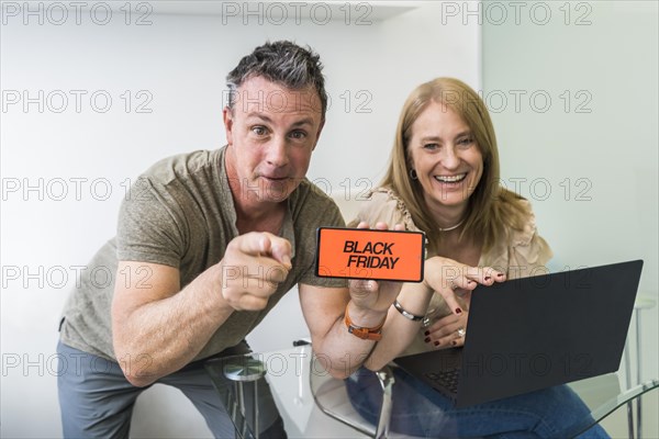 A man holds mobile phone with Black Friday advertisement on the screen with her wife on his side