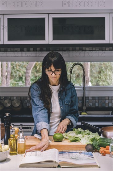 Woman reading recipe while preparing food in the kitchen. Vertical shot. Copy space