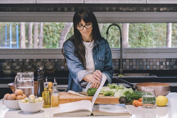 Mid-adult woman reading recipe while preparing food in the kitchen