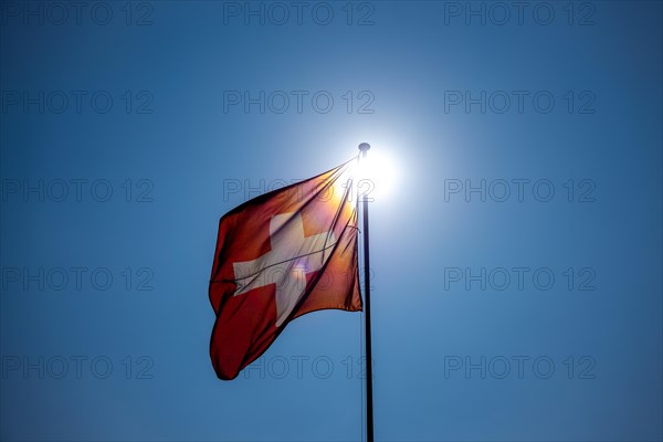 Beautiful Swiss Flag Against Blue Clear Sky and the Sun in a Windy Day in Switzerland