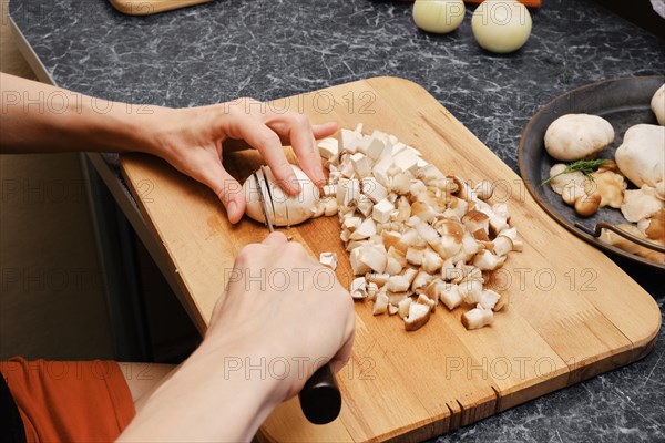 Unrecognizable woman cutting champignon on wooden cutting board in the kitchen