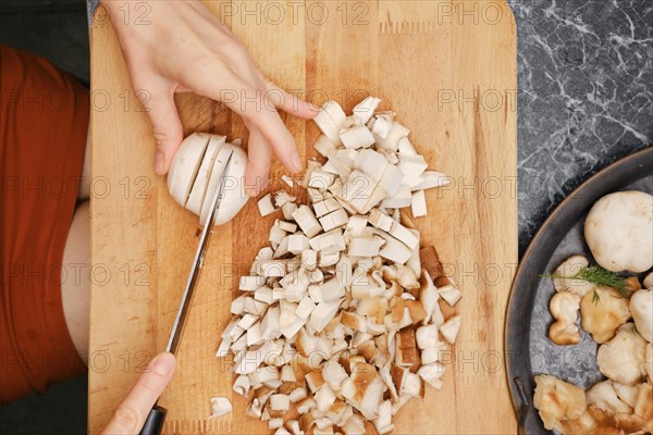 Overhead view of female hands cutting champignon on wooden cutting board