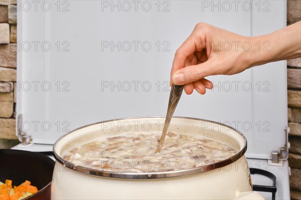 Unrecognizable woman mixing soup in a casserole on a stove
