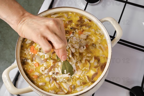 Top view of hand of woman adding bay leaf to soup on a gas stove