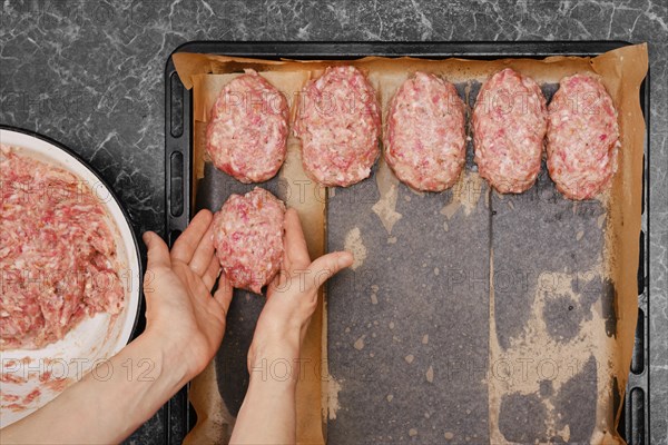 Unrecognizable woman put beef meat patties on baking tray