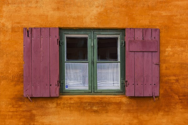 Wooden window with window flaps in front of orange facade