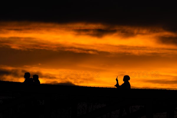 A passer-by takes a photo with her smartphone from the Eiserner Steg in Frankfurt am Main towards the sunset.