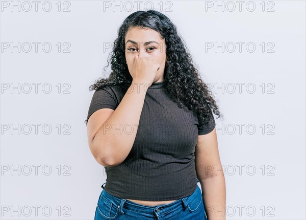 Displeased girl holding her nose isolated. Disgust people covering nose. Latin woman covering nose from a bad smell isolated