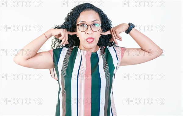 Displeased afro woman covering ears and sticking out tongue isolated. Latin woman covering her ears and making faces isolated