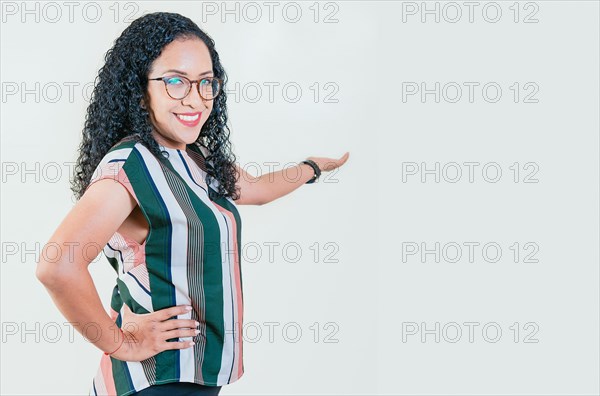 Smiling young afro woman welcoming you isolated. Happy afro girl pointing back presenting a product isolated. Cheerful people pointing a promotion with her palm