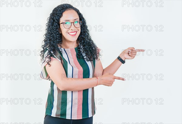 Cheerful afro girl pointing an offer isolated. Beautiful latin girl pointing to a banner to the side. Happy young afro woman pointing a promotion at side
