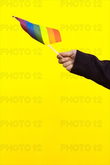 Hand holding lgbt flag in yellow background. A hand holding rainbow flag on isolated background