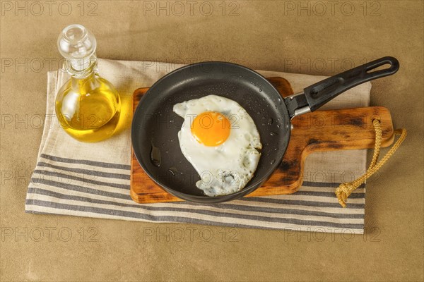 Fried egg with extra virgin olive oil in a frying pan with a glass bottle with oil on a wooden board