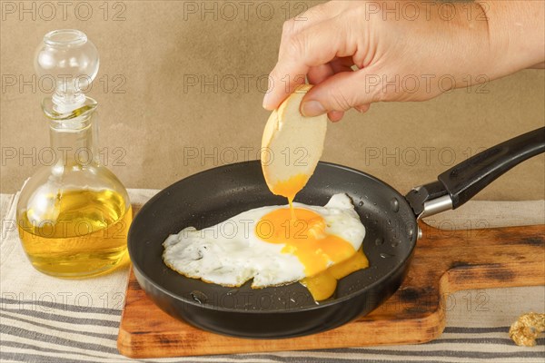 Woman hand Dipping bread on the yolk of an egg fried in olive oil with a frying pan on a wooden board