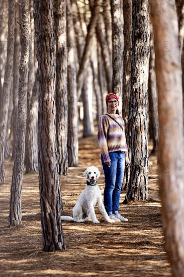 Woman with white poodle in a pine forest
