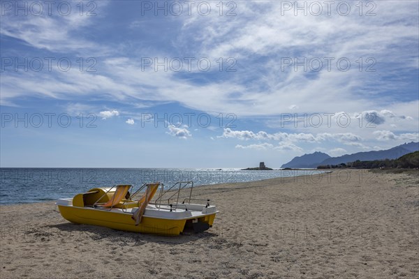 Yellow pedal boat on the beach in front of the Torre Di Bari Sardo tower in the distance