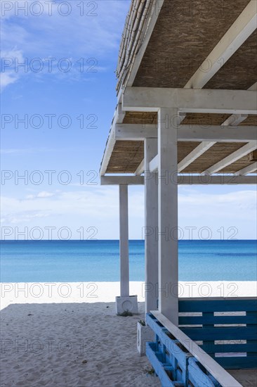 White hut with thatched roof on a white sandy beach and blue sea