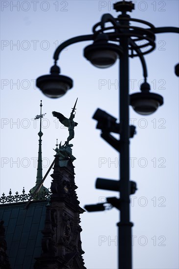 Angel figure with sword on the roof of the town hall fighting against a pole with lamps and video cameras